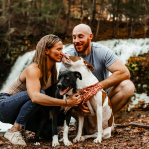 happy couple with two dogs in front of waterfall professional pet photography